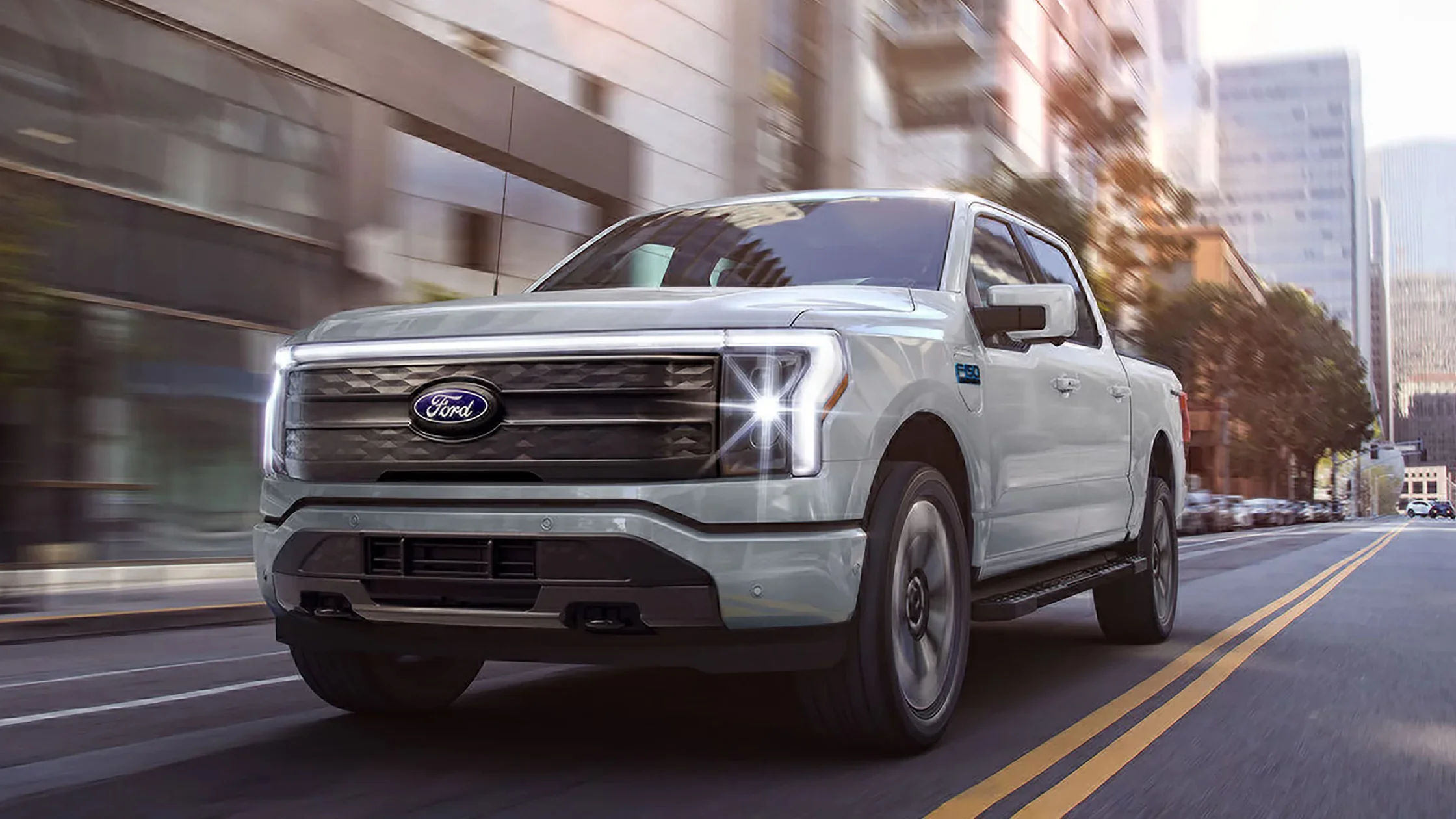 Front view of a 2024 Ford F-150® Lightning driving on a city street with LED headlights illuminated.