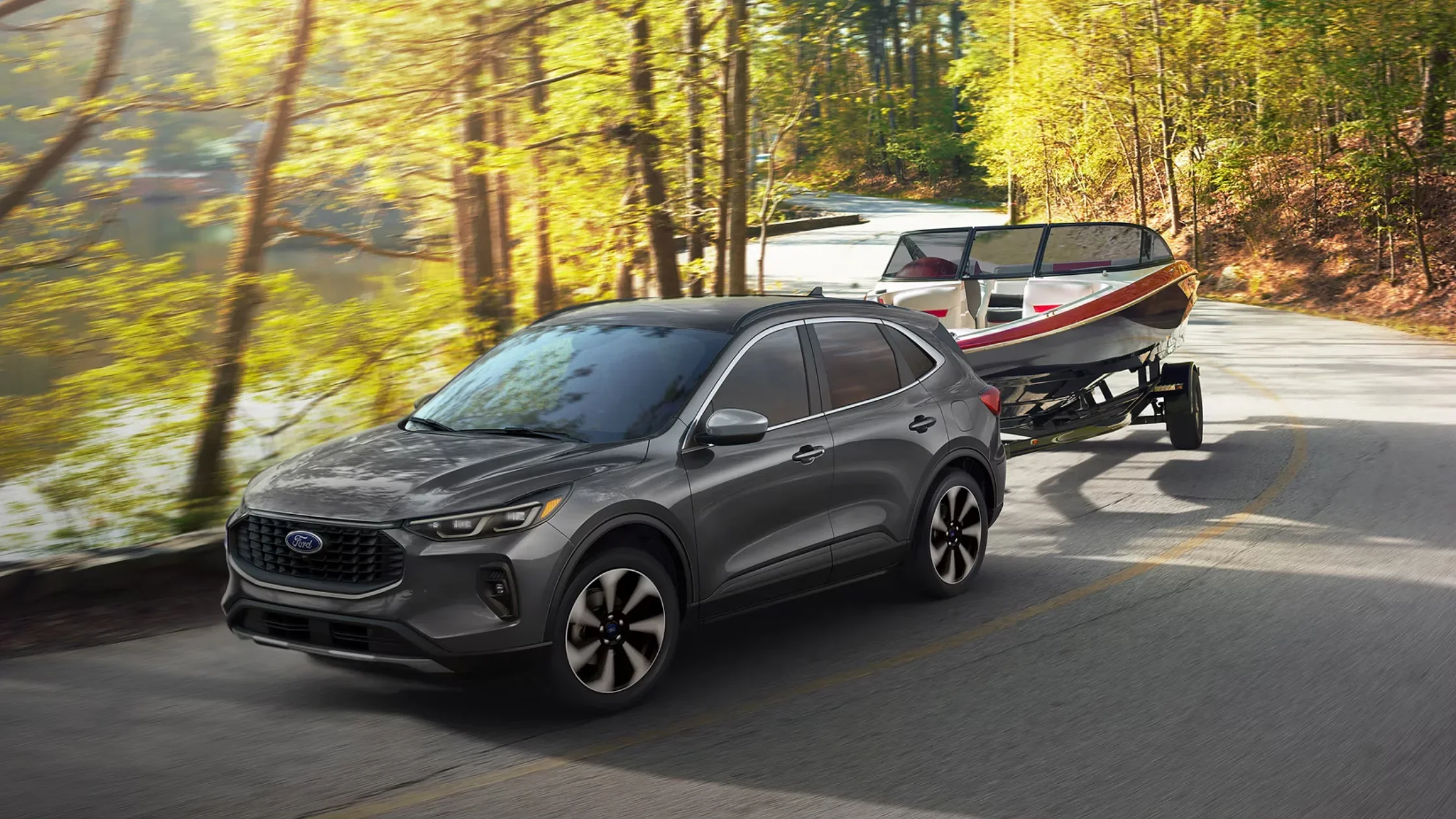2025 Ford Escape® towing a speedboat through a wooded lakeside road in daylight