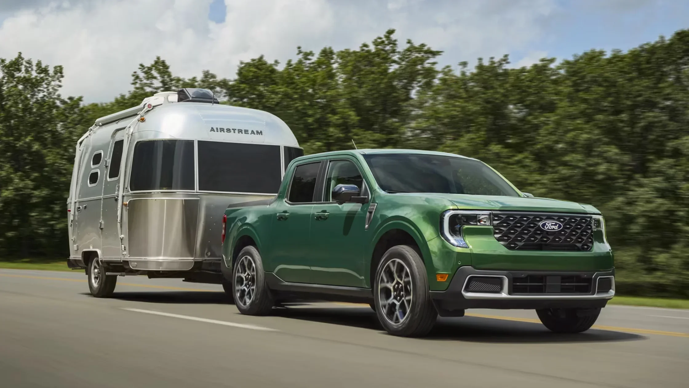 2025 Ford Maverick® in green towing an Airstream trailer on a highway with trees in the background.