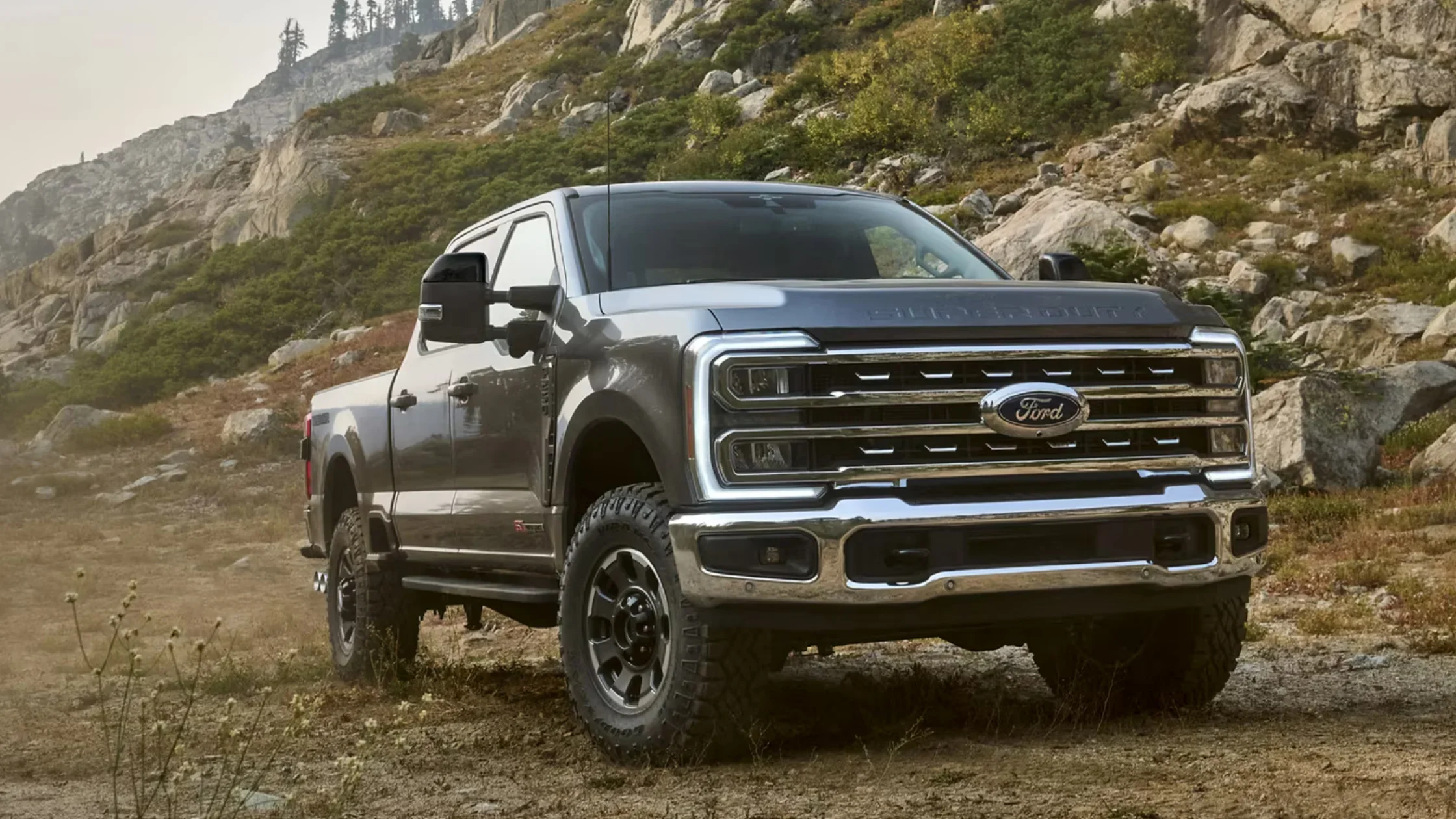 2025 Ford Super Duty® off-roading on rocky terrain with chrome grille and rugged tires.